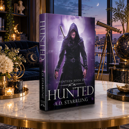 Hunted (Seventeen Book 1) Hardback by A.D. Starrling on a marble table with a telescope and the Boston skyline at dusk