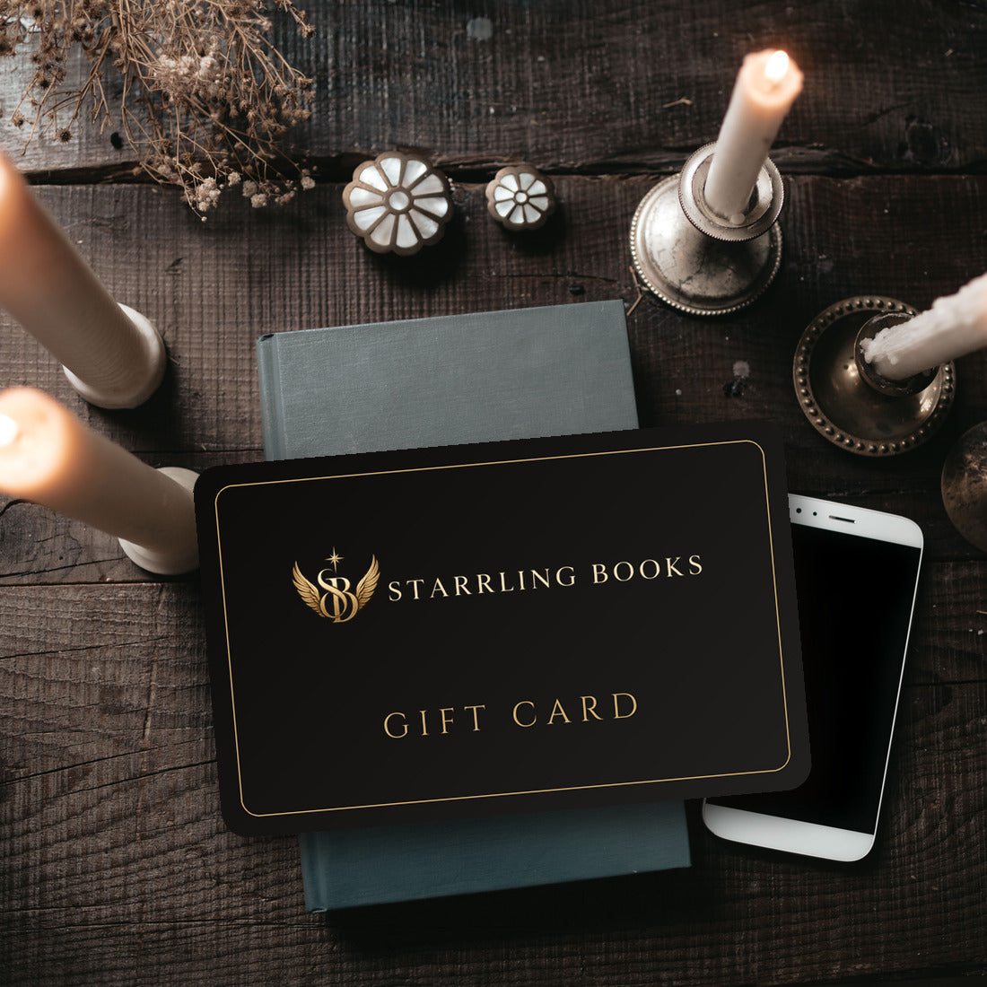 Starrling Books gift card resting on a book beside candles on a dark wooden table